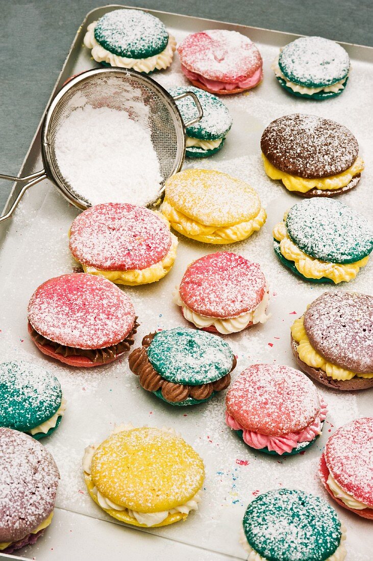 Various macaroons dusted with icing sugar on a baking tray