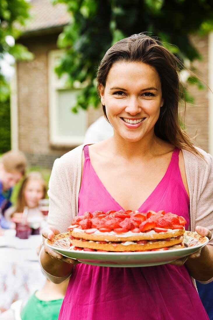 A young woman holding a strawberry cake