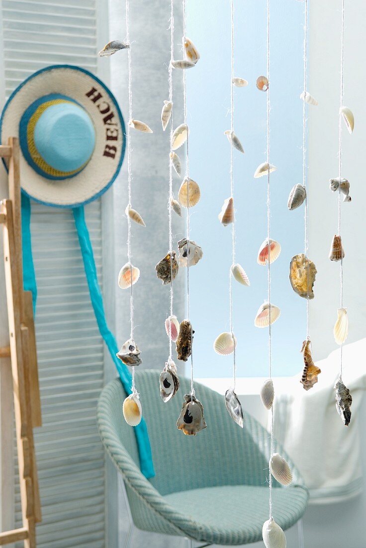 Seashells strung on cords hanging from ceiling in front of wicker chair