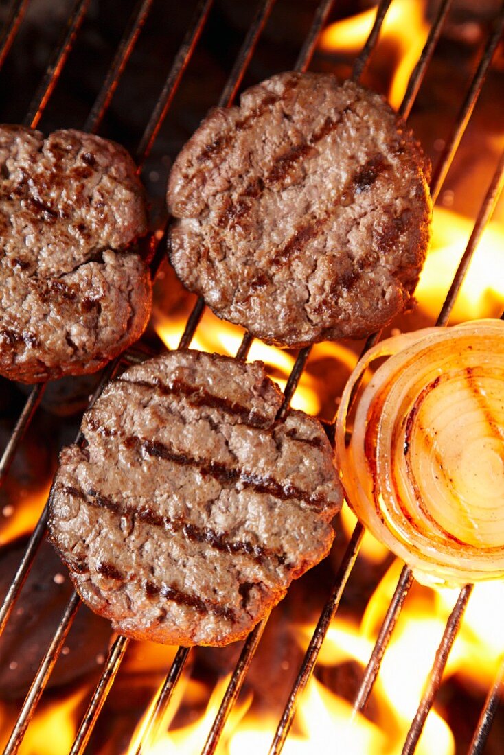 Büffel-Hacksteaks auf Grillrost über Grillfeuer