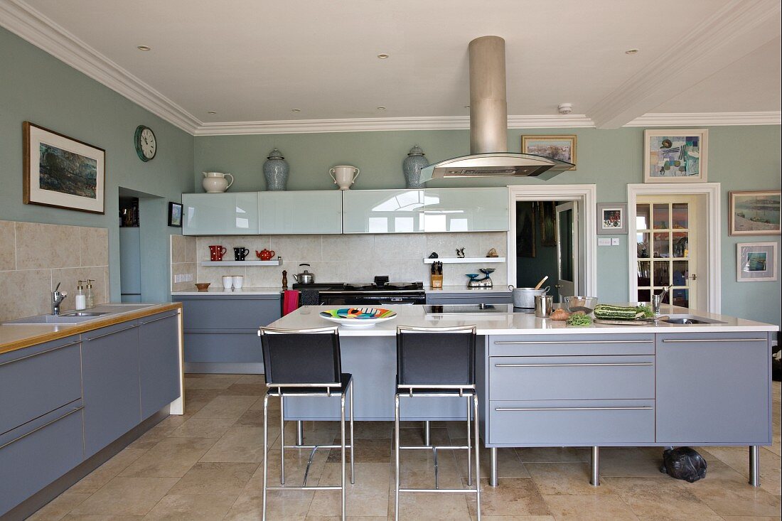 Large, modern kitchen with blue-grey cupboard doors and bar stools at free-standing kitchen island in country-style atmosphere