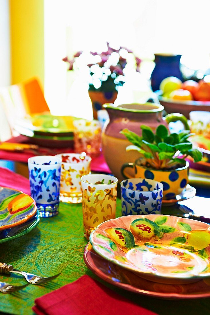 Colourful dining table with brightly painted ceramic crockery and patterned glasses
