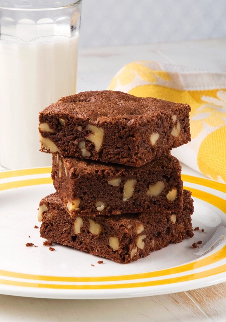 Three Walnut Brownies Stacked on a Plate; Glass of Milk