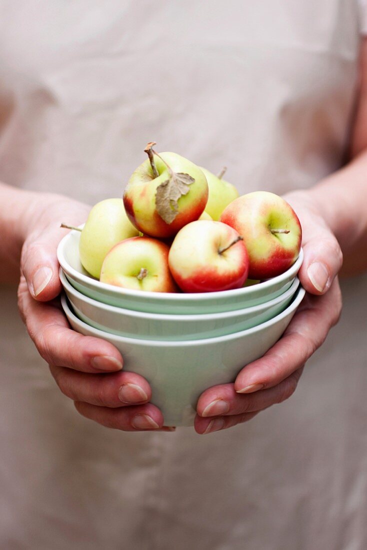 Hands holding a stack of bowls with apples