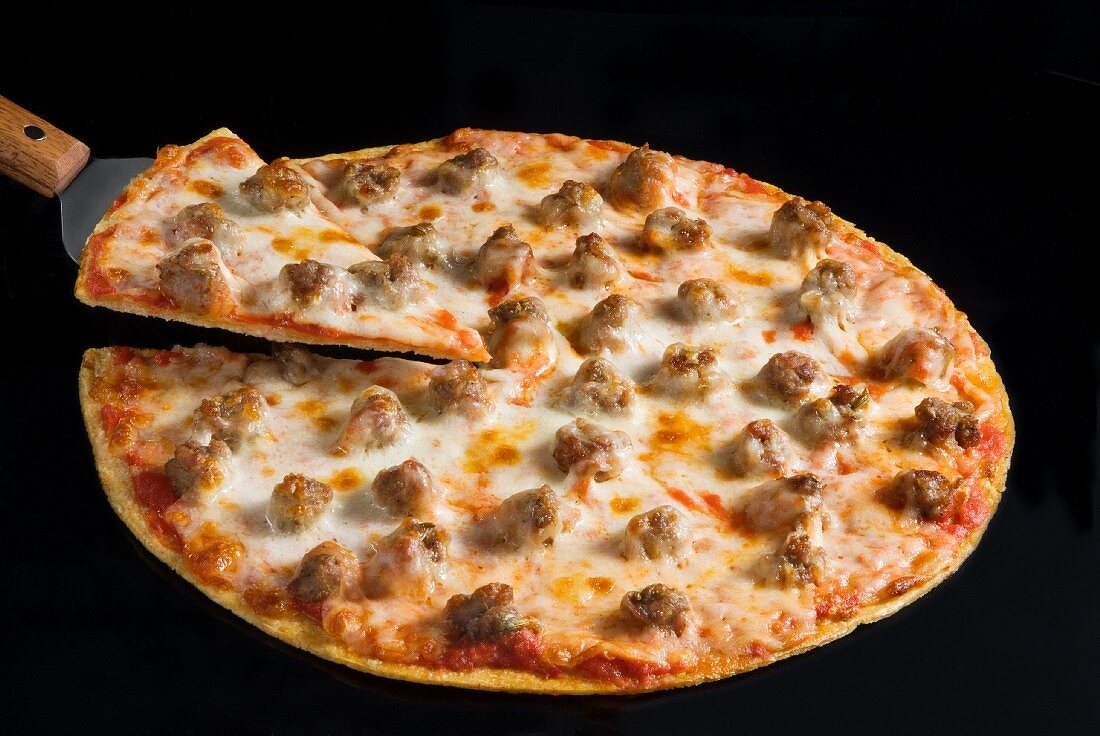 Thin Crust Sausage Pizza on a Black Background with a Slice on a Spatula