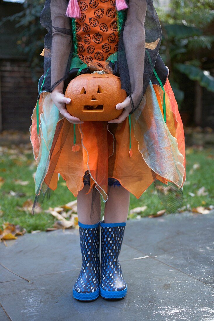 Frau in Kürbiskostüm hält Halloween-Kürbis in den Händen