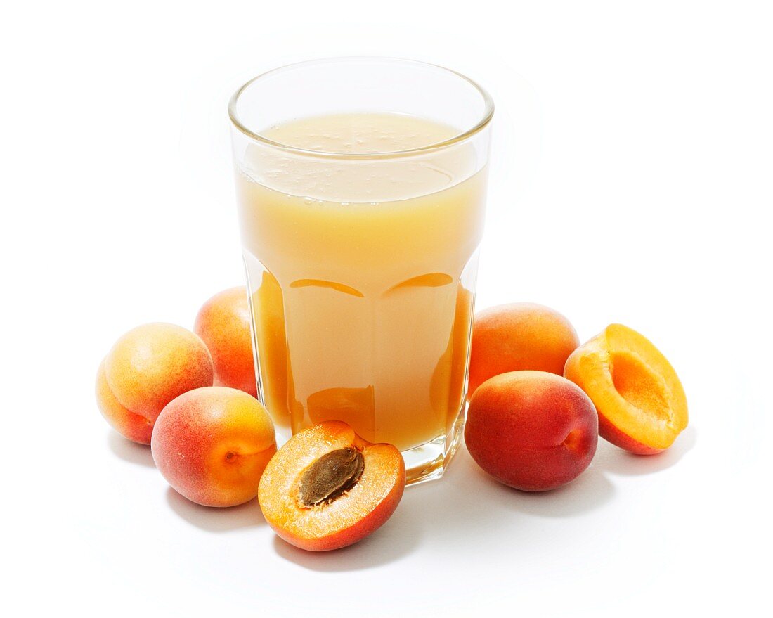 A glass of apricot juice surrounded by whole and halved apricots