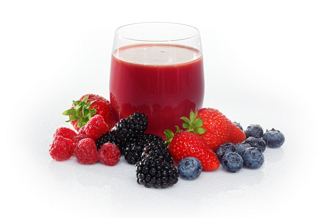 A glass of fruits of the forest juice surrounded by fruits of the forest