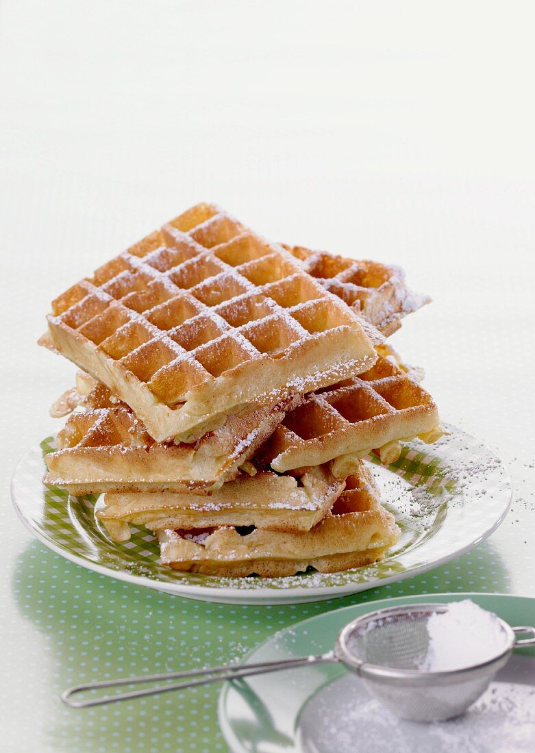 A stack of waffles dusted with icing sugar