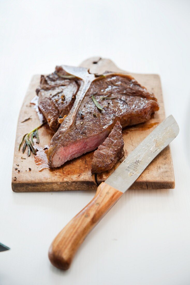 A T-bone steak on a wooden board with a knife