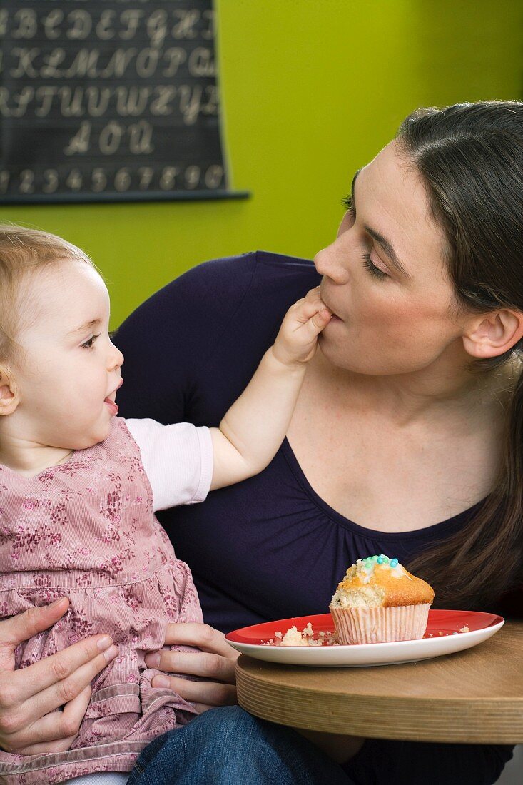 Kleines Mädchen füttert ihre Mutter mit Cupcake