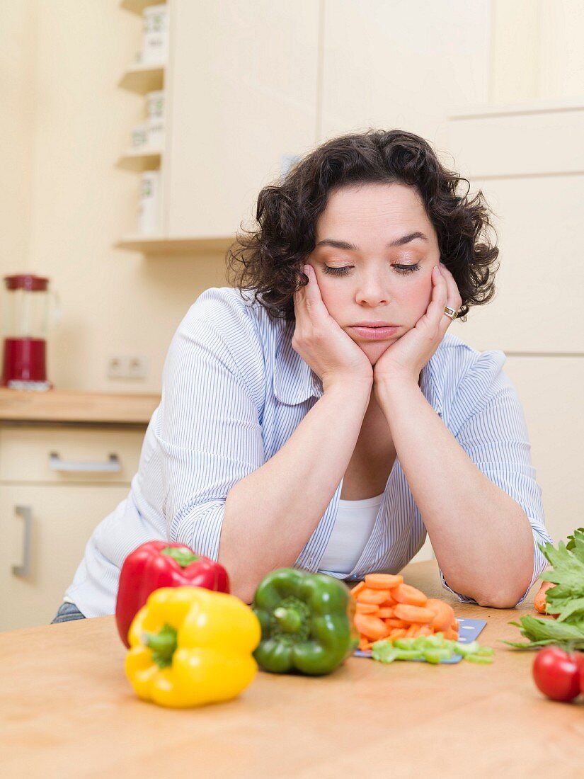 Frau schaut gelangweilt auf Gemüse in der Küche