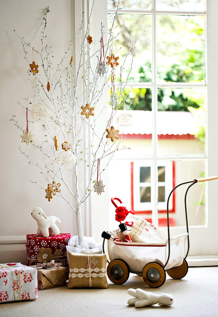 Various Christmas presents, toys and gifts in dolls' pram; Christmas biscuits as decorations on small, white-painted tree