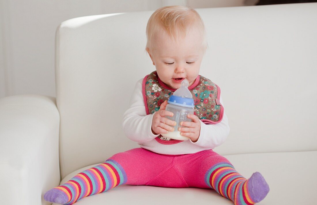 Baby mit Milchflasche auf Sofa sitzend