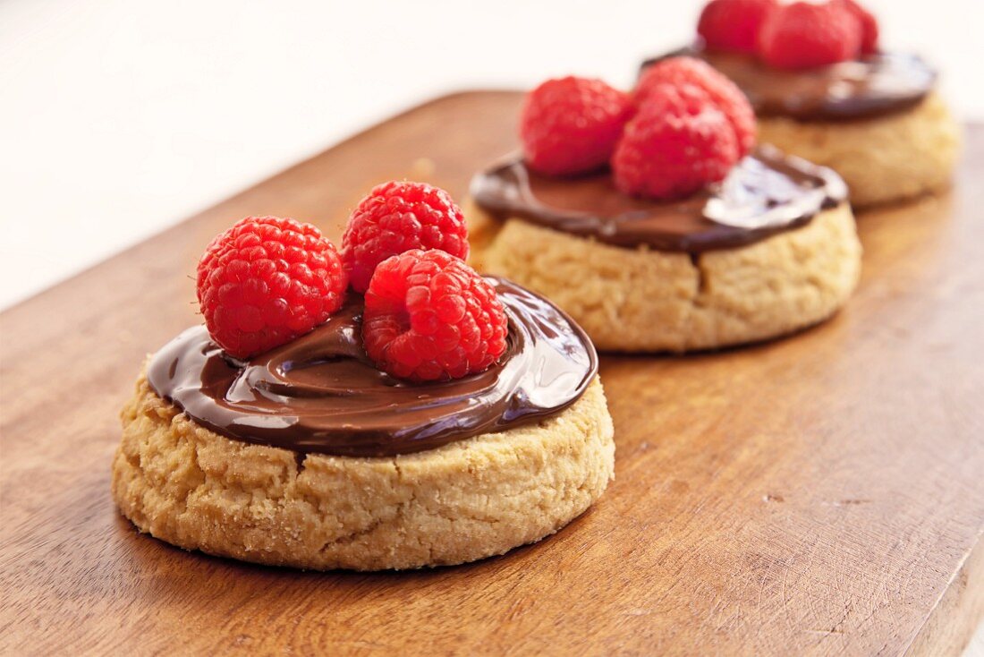 Plätzchen mit Nougatcreme und Himbeeren auf Schneidebrett