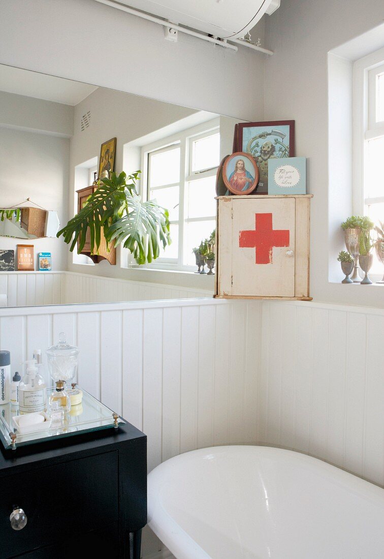Detail of bathroom corner with bathtub against white, half-height wooden wall and first aid cabinet in corner