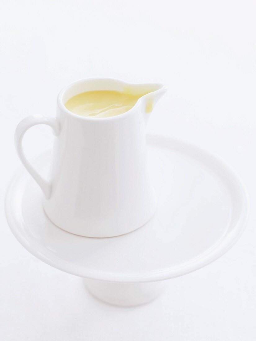Custard cream in a small white pitcher on a cake stand