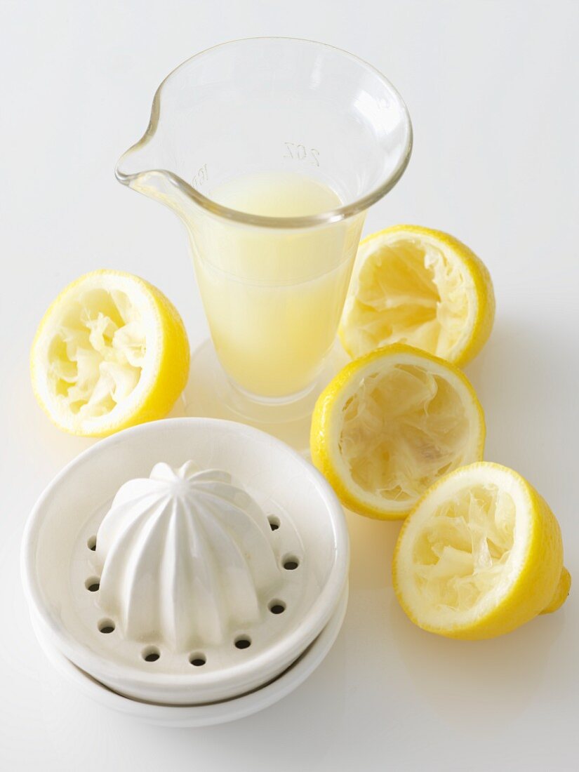 Zitruspresse, ausgepresste Zitronen und ein Krug frisch gepresster Zitronensaft