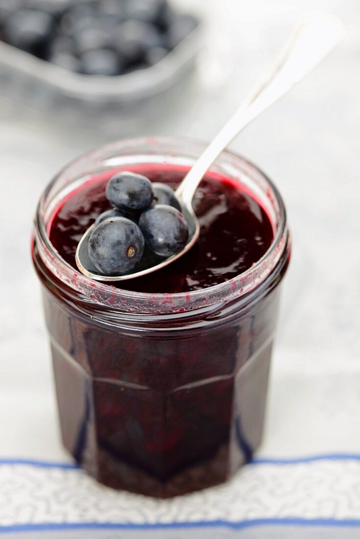 A jar of blueberry jam with spoon and fresh blueberries