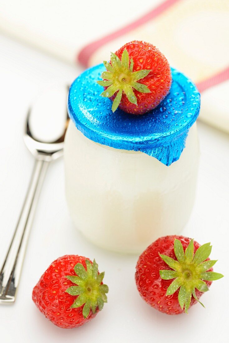 Natural yogurt in a glass surrounded by fresh strawberries