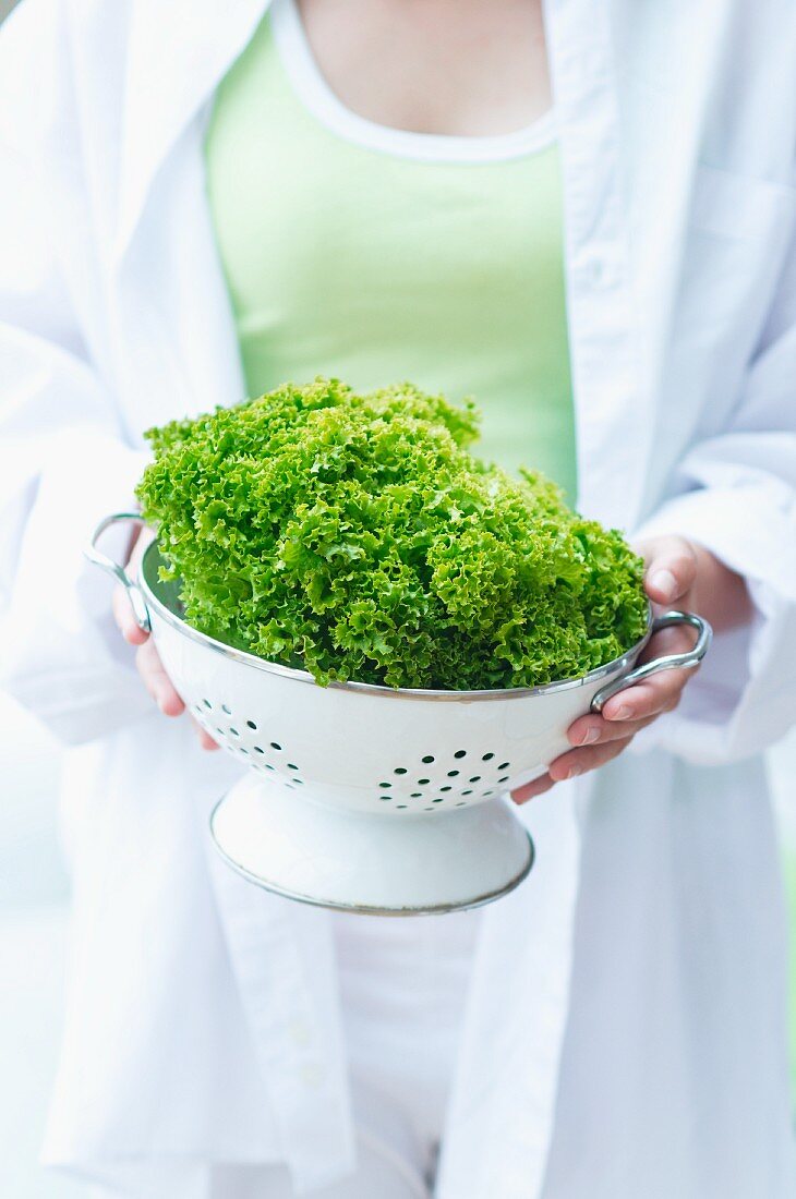 A young woman holding a colander of lollo biondo lettuce