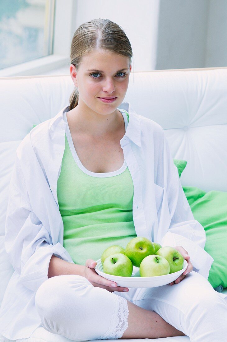 A girl holding a plate of green apples