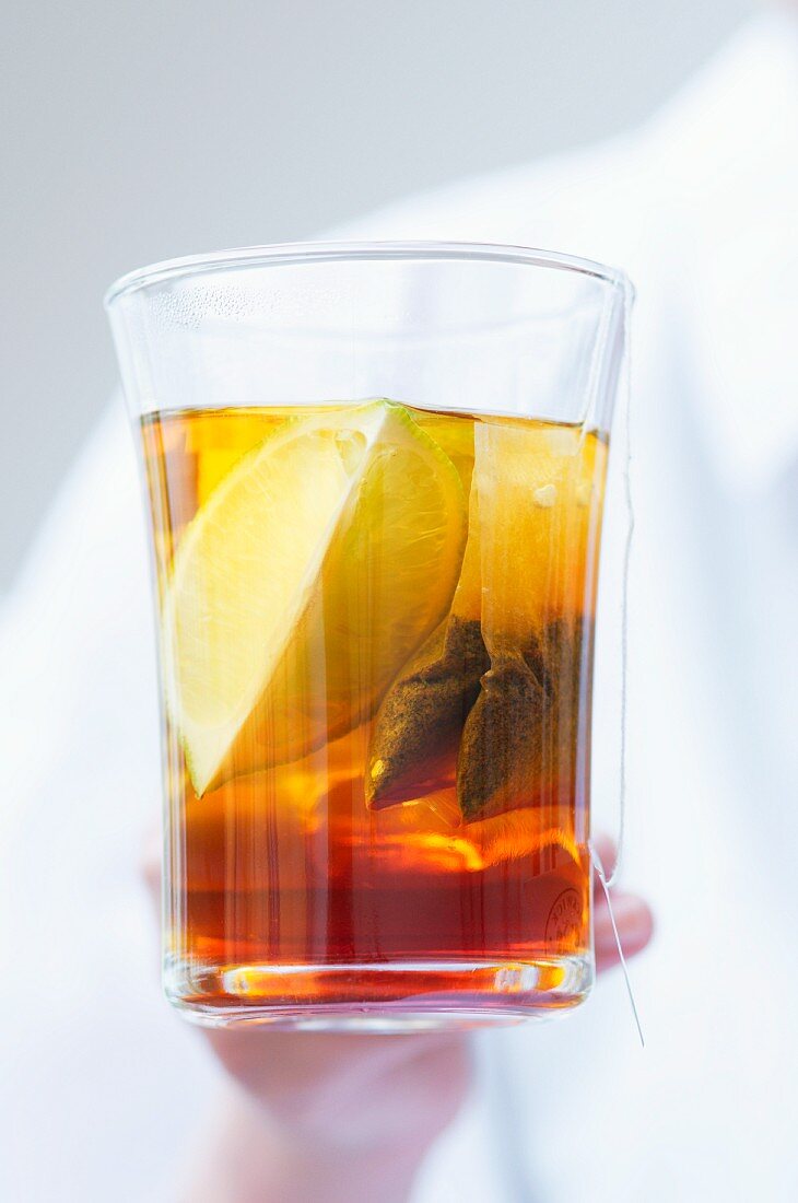 A glass of tea with a lemon wedge and a tea bag