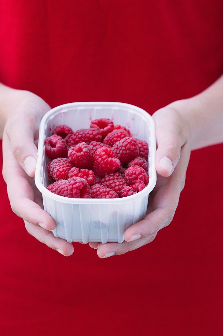 A girl holding a plastic bowl of raspberries