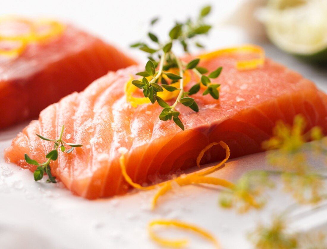 A raw salmon fillet on a bed of salt with lemon zest and dill flowers