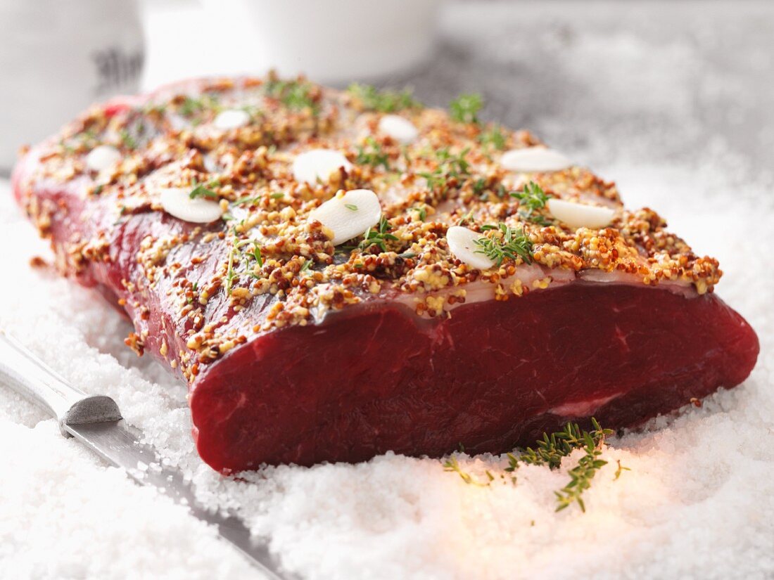 Raw beef loin with a mustard and garlic marinade on a bed of salt