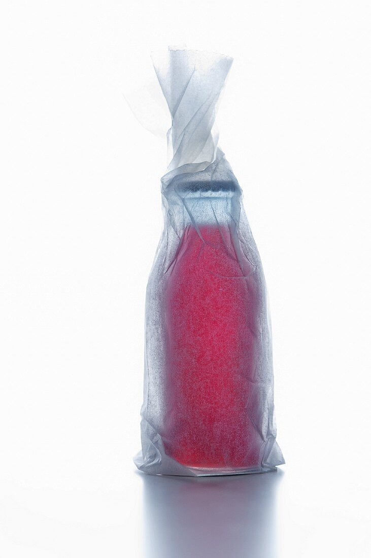 Flasche mit roter Flüssigkeit, in Papier verpackt