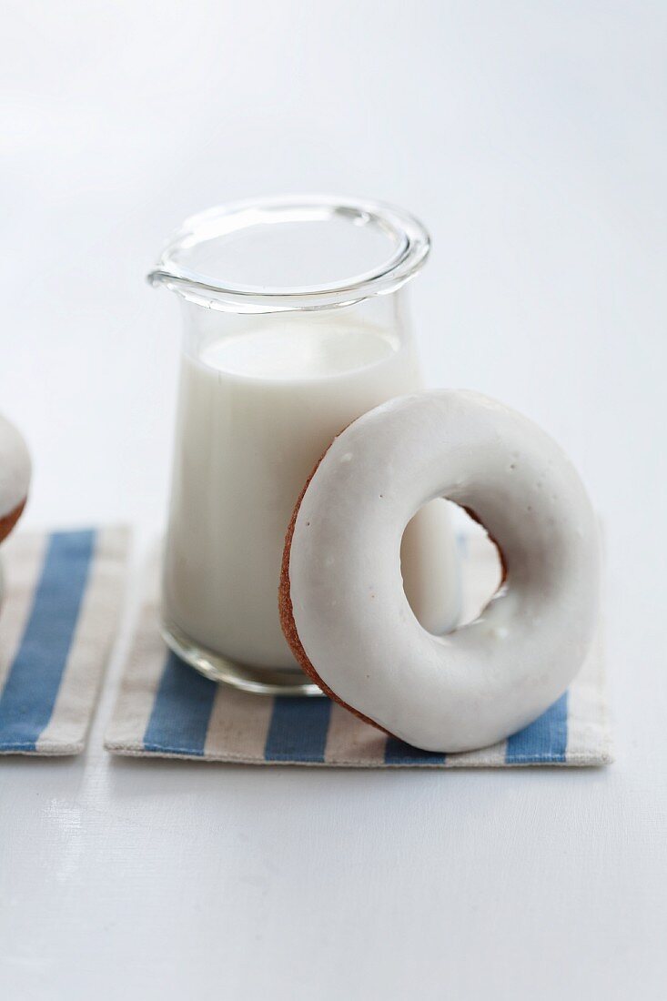 A doughnut with sugar icing leaning against a jug of milk