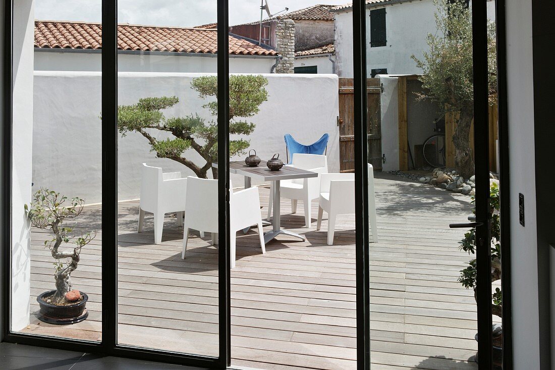 Blick durch eine Fensterfront auf die Terrasse mit Zierbäumchen und modernen Terrassenmöbeln