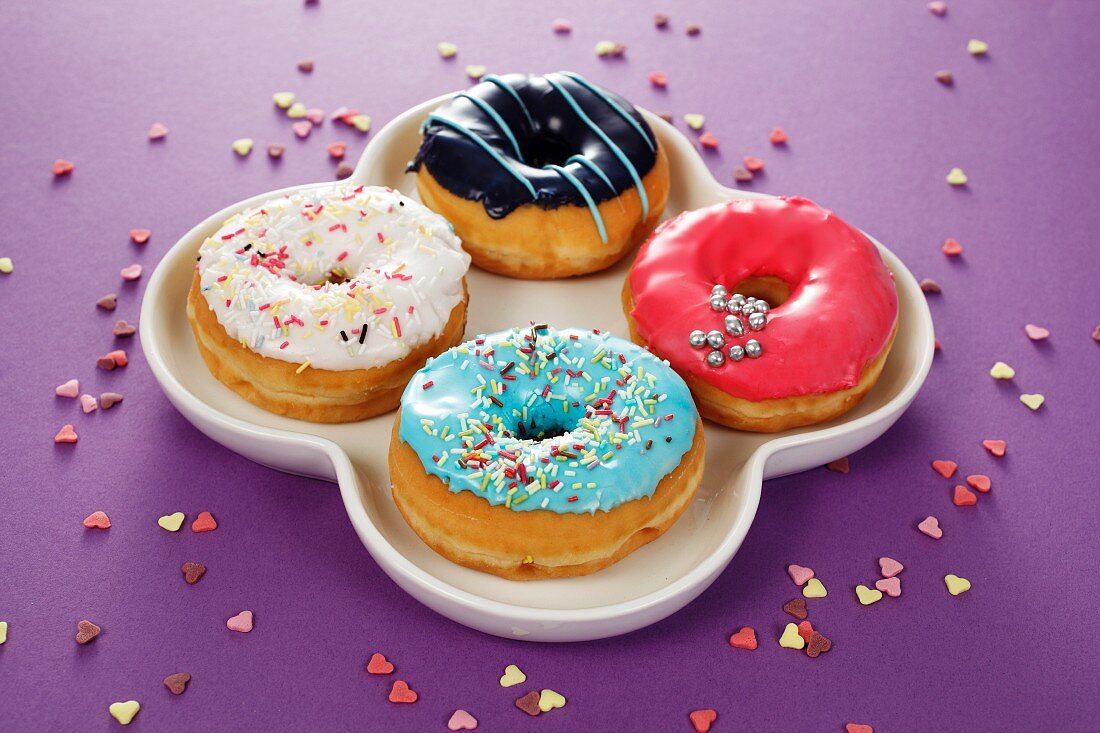 Four doughnuts with colourful glaze and sugar sprinkles