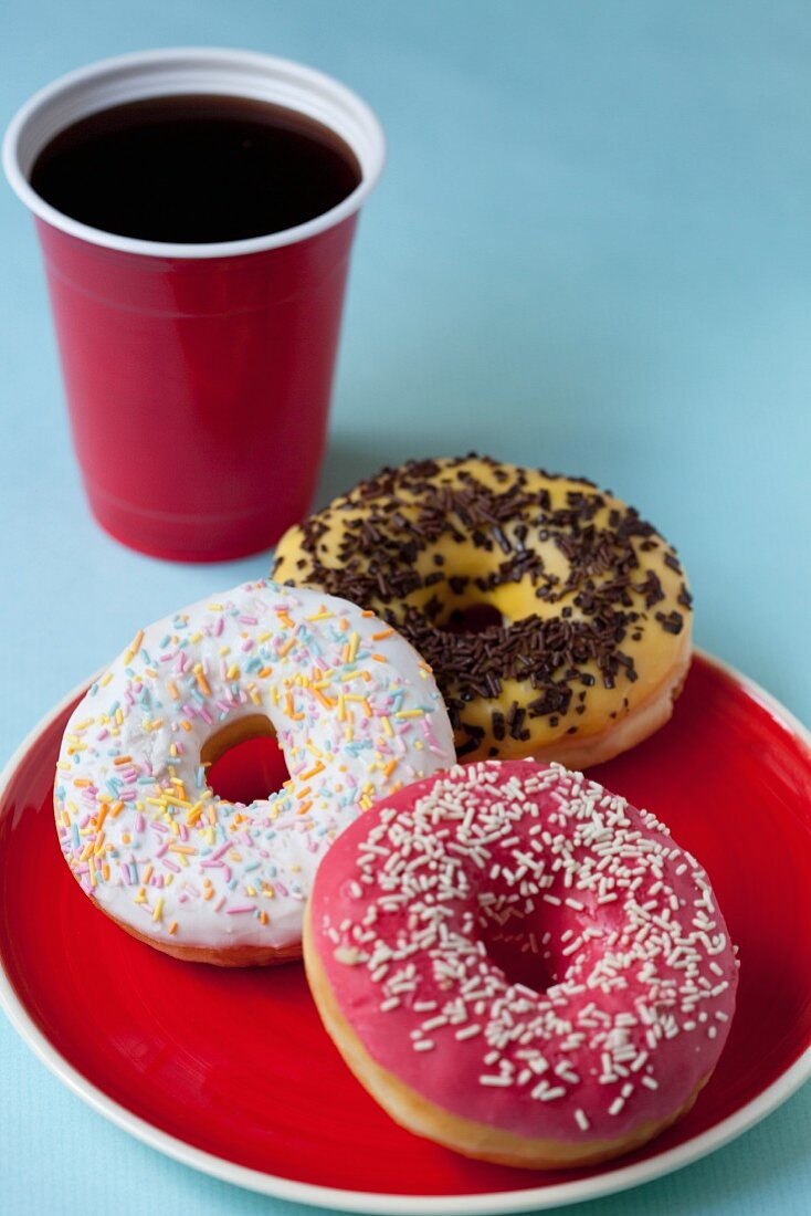 Glazed doughnuts with sugar and chocolate sprinkles and a cup of coffee