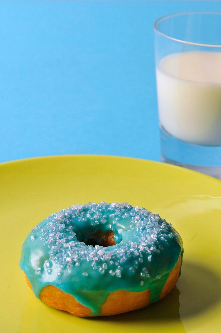 A doughnut with blue glaze and a glass of milk