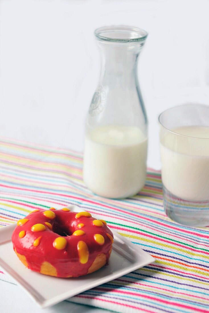 A doughnut with red and yellow glaze and a glass of milk