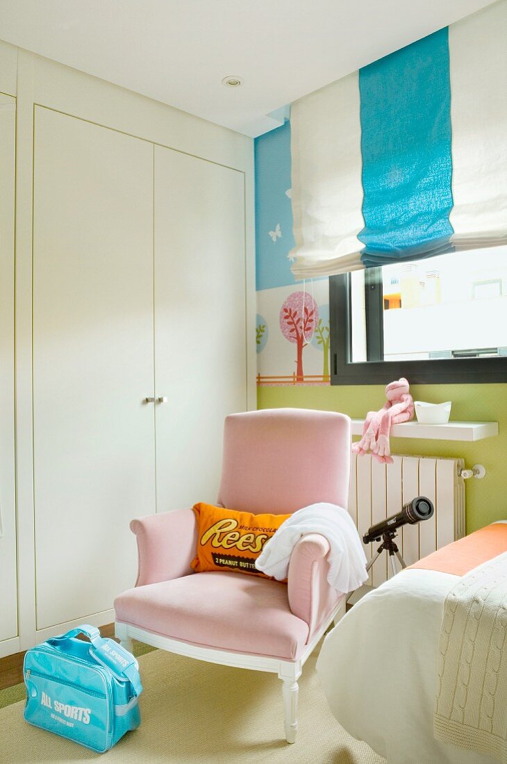 Rosa gepolsterter Sessel vor Einbaukleiderschrank und Faltrollo mit Blockstreifen in pastelfarben gestaltetem Kinderzimmer