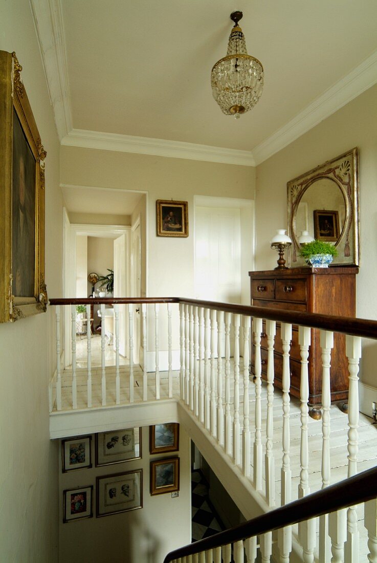 Elegant landing with small gallery area, dark chest of drawers on white wooden floor and view into living area through open interior door