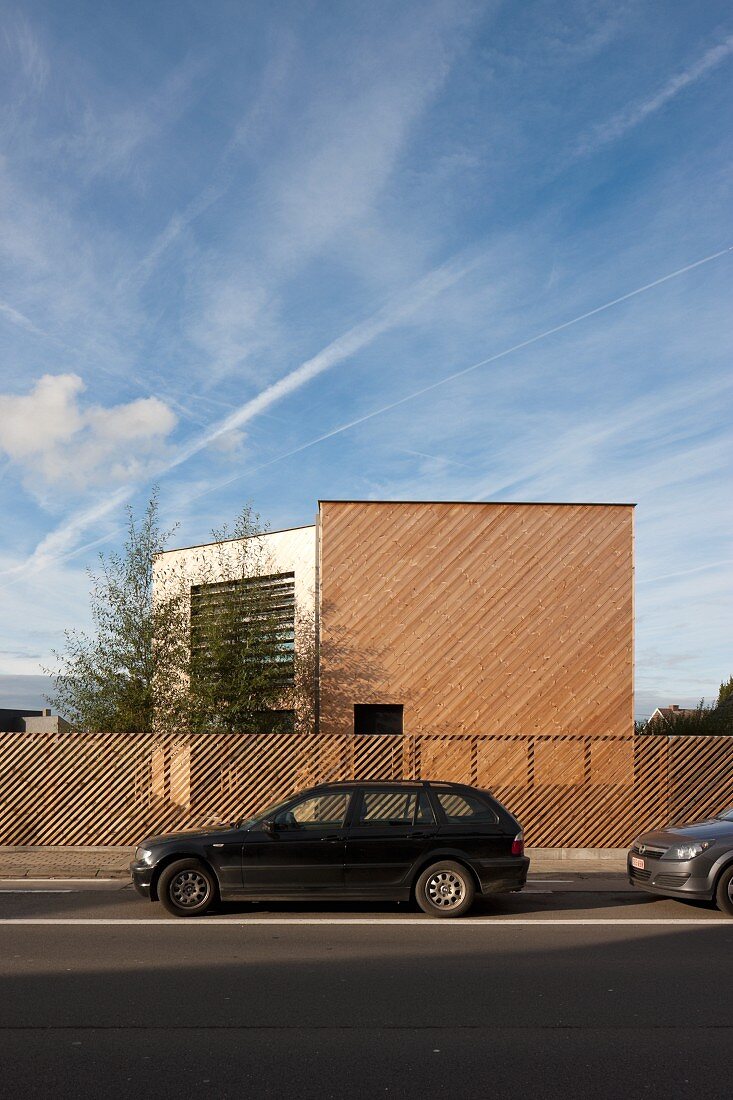 Blick über Strasse auf zeitgenössisches Wohnhaus aus Holz und Gartenzaun