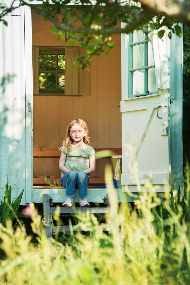 Mädchen sitzt auf Holzstufen eines Gartenhäuschens