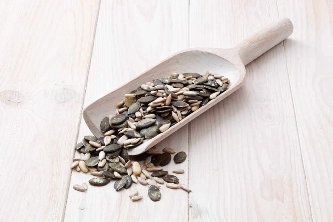 Sunflower seeds, pumpkin seeds and pine nuts on a wooden scoop