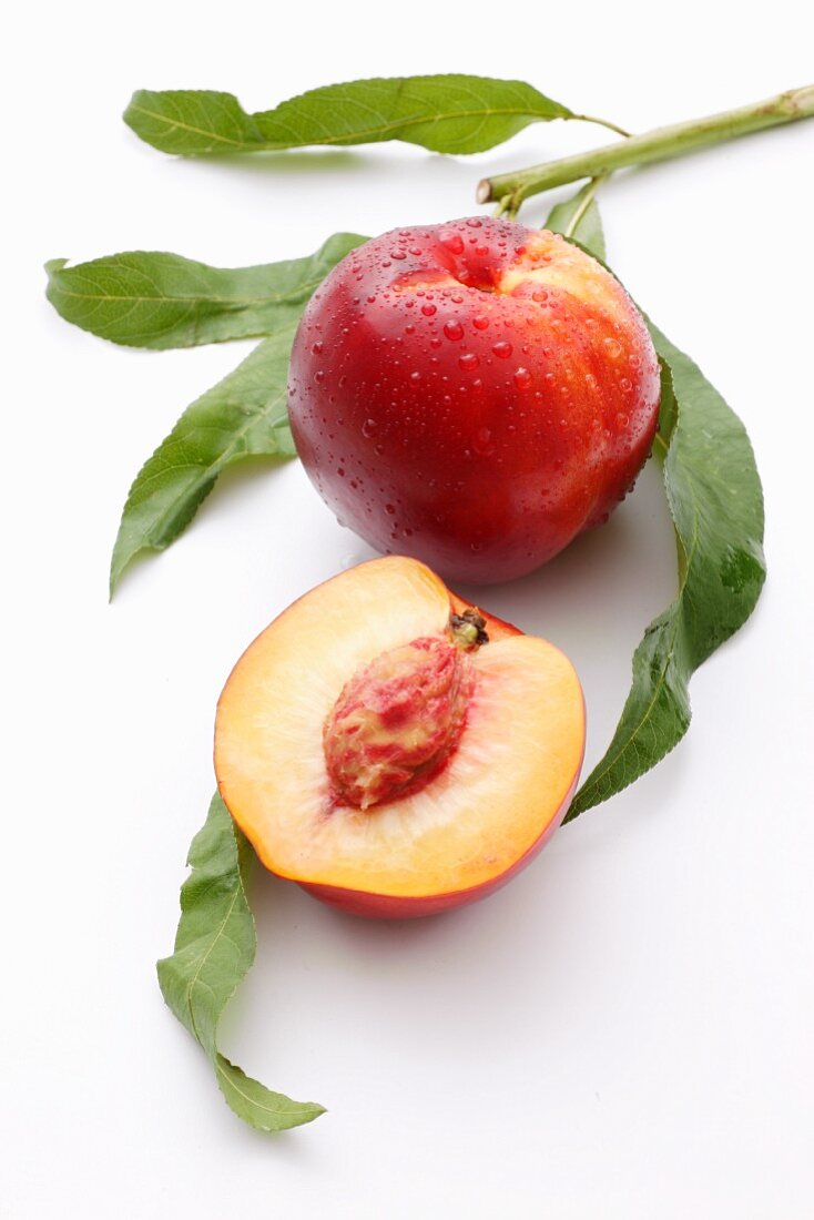 A whole nectarine and half a nectarine with leaves