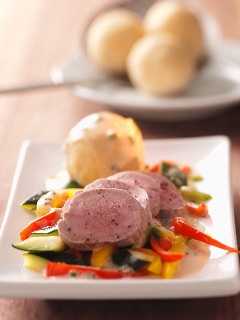 Pork fillet on bed of colourful vegetables with potato dumplings and caper sauce