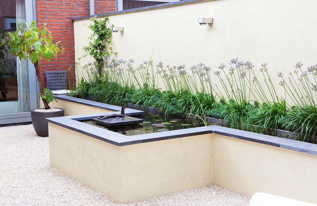 Wasserbecken mit Schmucklilien und Wasserpflanzen; in der Mitte eine bronzene Skulptur