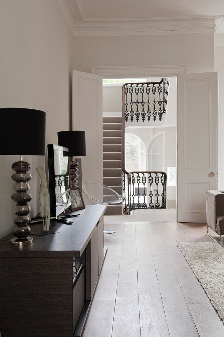 Two table lamps and TV on sideboard with view of stairwell in background