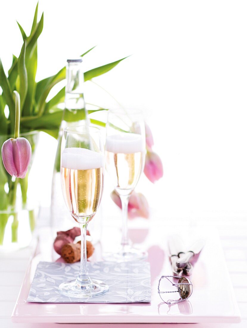 Two glasses of sparkling wine with a vase of tulips