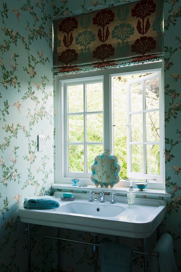 Vintage washstand below window in corner of bathroom with floral wallpaper