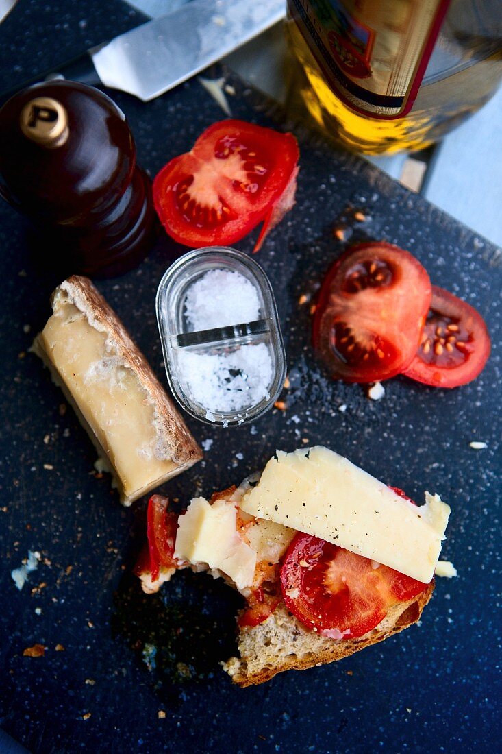 A slice of cheese and tomato bread with a bite taken out on a table with ingredients