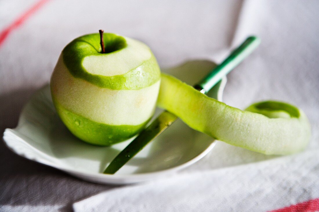 Teilweise geschälter grüner Apfel auf Teller mit Messer